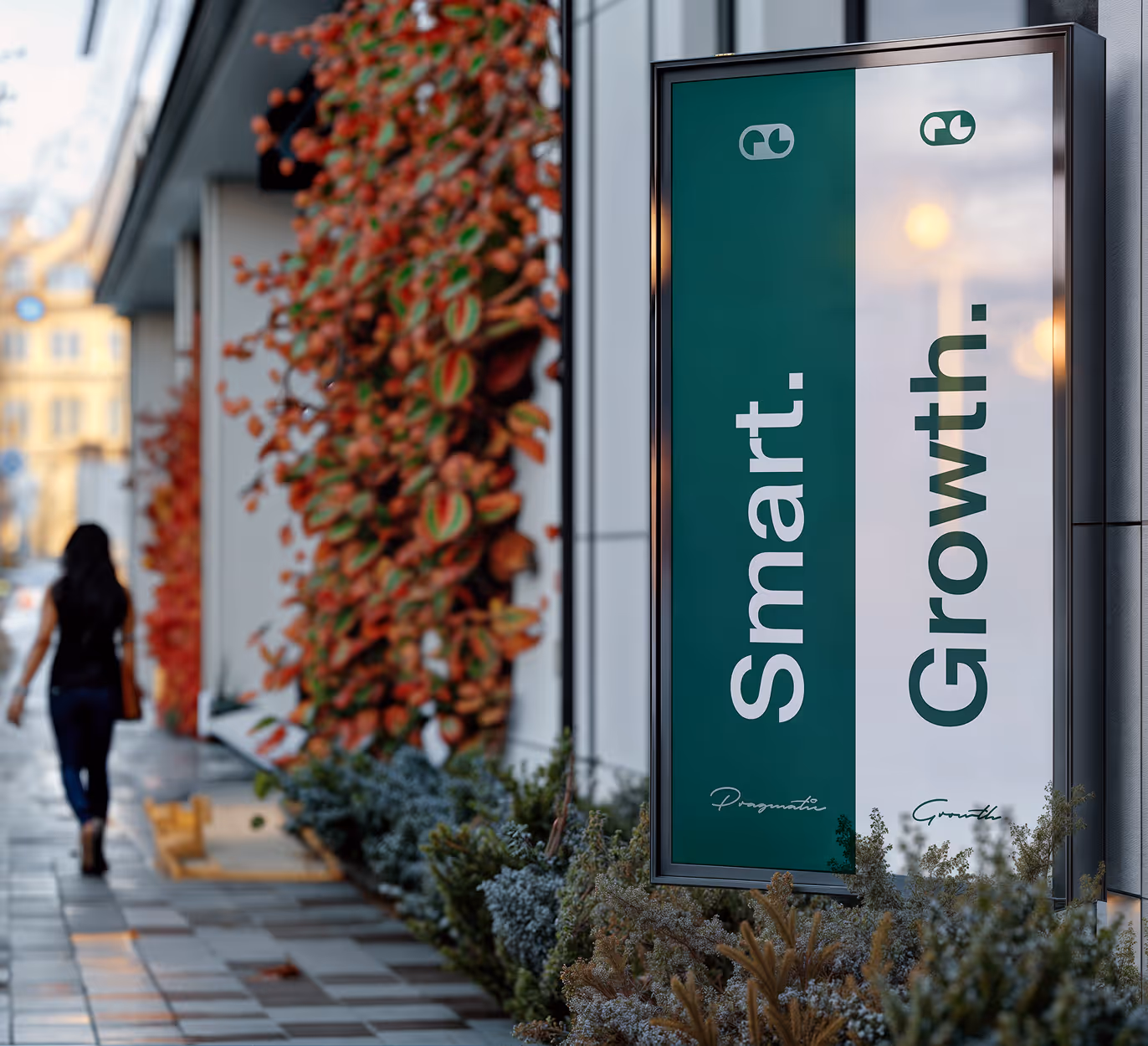 Outdoor sidewalk view with a vertical sign displaying the words 'Smart. Growth.' in white and green panels beside a wall covered with red and green foliage.
