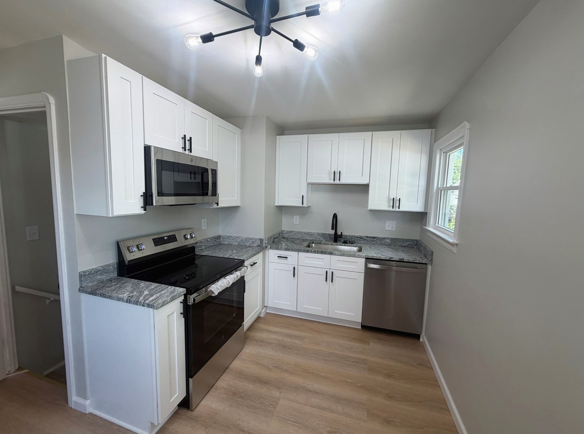 Renovated white kitchen with stainless appliances and wood-look floors, Wayland Ave Cleveland renovation