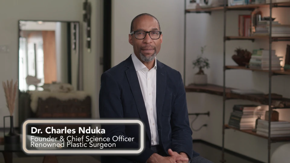 Dr. Charles Nduka, Founder & Chief Science Officer and Renowned Plastic Surgeon, smiles wearing glasses and a suit jacket, in an indoor setting.