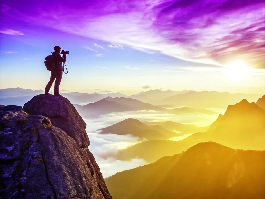 A lone hiker capturing a breathtaking mountain landscape at sunrise, showcasing the beauty of adventure photography.