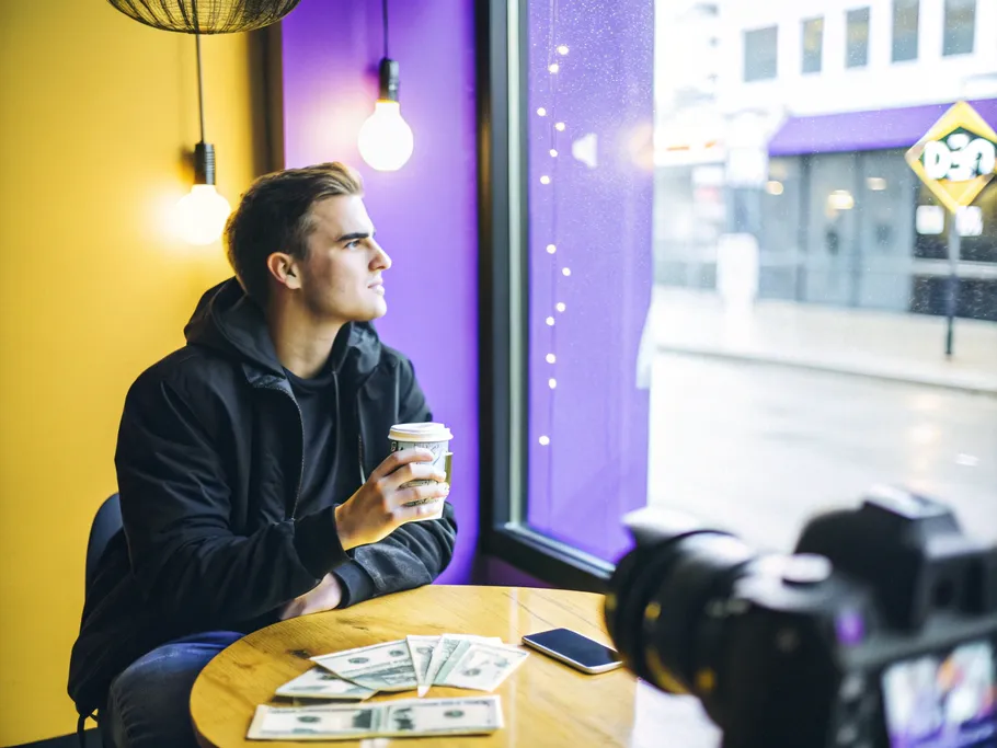 An influencer in a coffee shop contemplating while holding a coffee cup, surrounded by production elements.