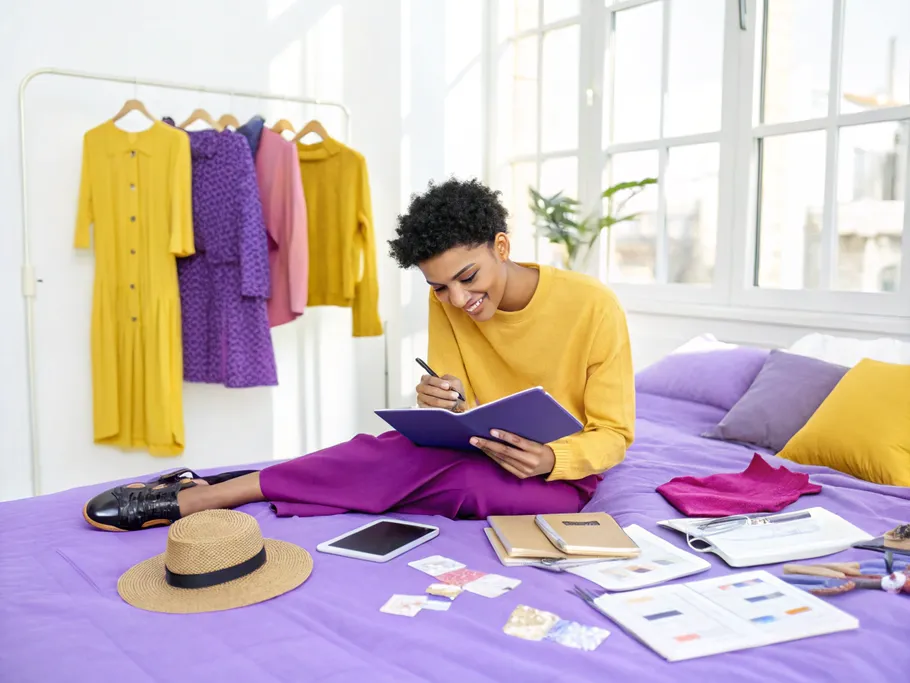 A confident content creator sketching ideas surrounded by stylish outfits and accessories.