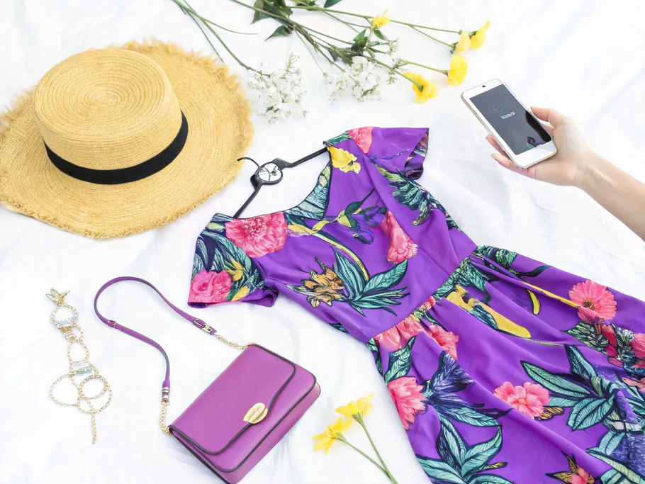 Chic summer flat lay featuring a floral dress, straw hat, sunglasses, handbag, and jewelry.