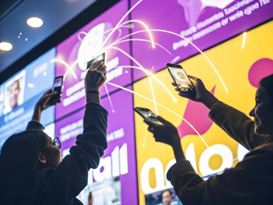 Hands holding smartphones engaging with a vibrant social media wall, symbolizing active customer engagement.