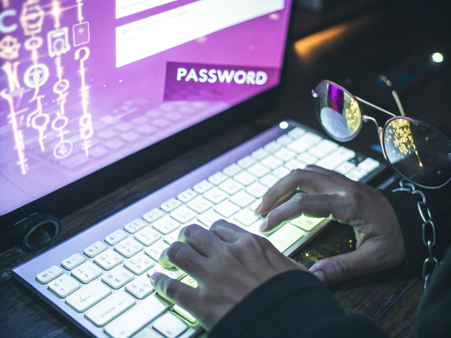 Close-up of hands typing on a backlit keyboard with a password field on the screen.