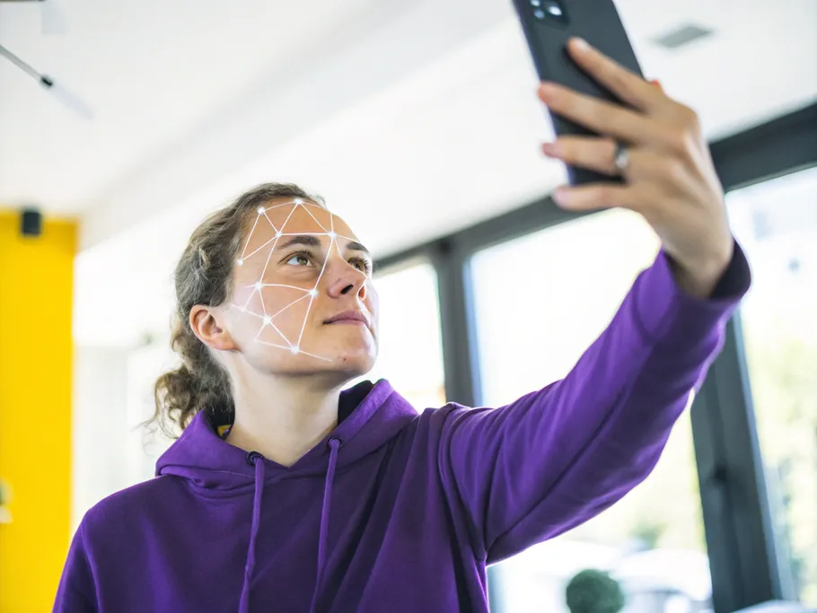 A gender-neutral person taking a video selfie with a smartphone, depicting digital identity verification.