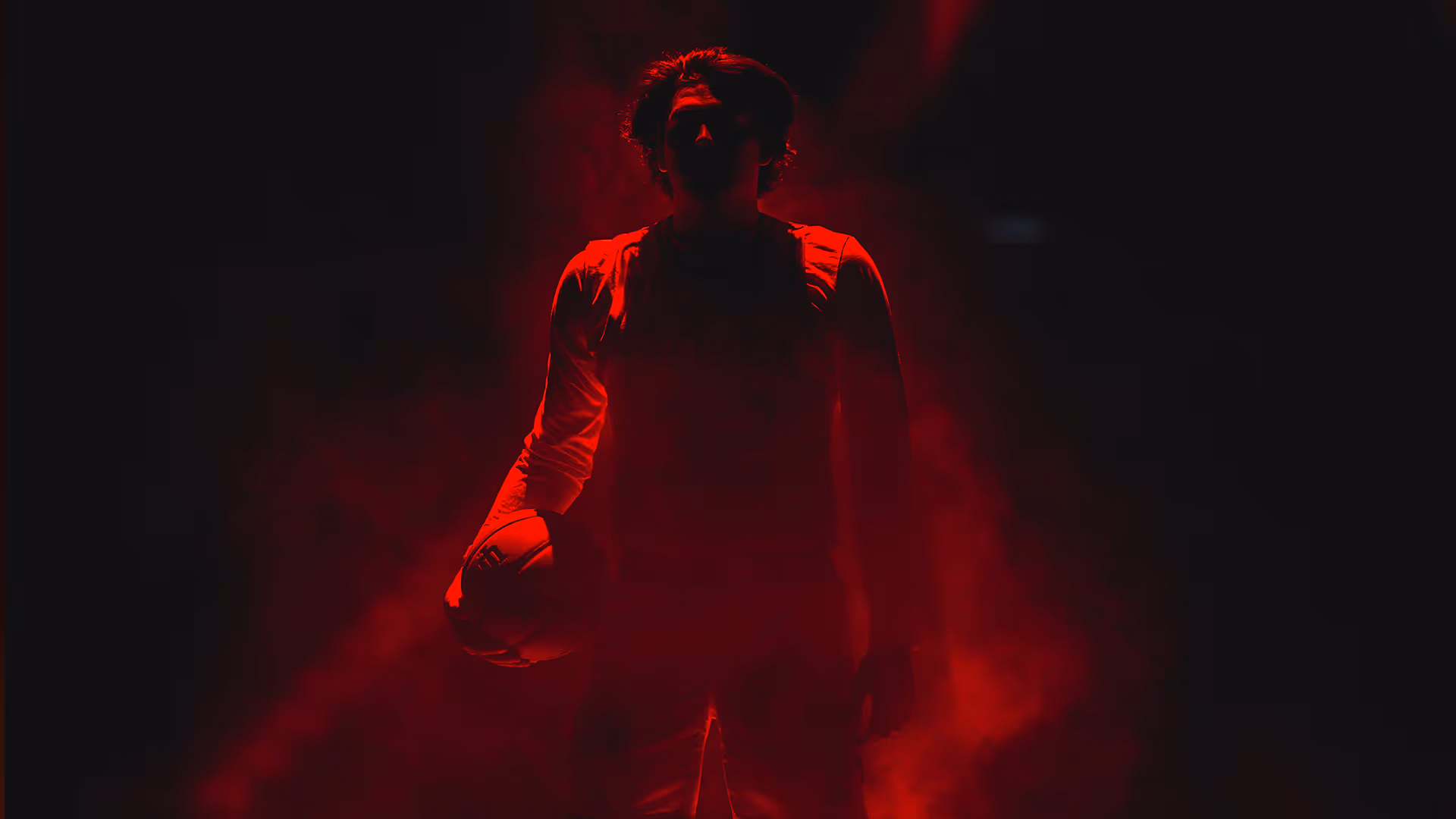 Silhouette of a basketball player holding a ball, illuminated by red light and smoke.