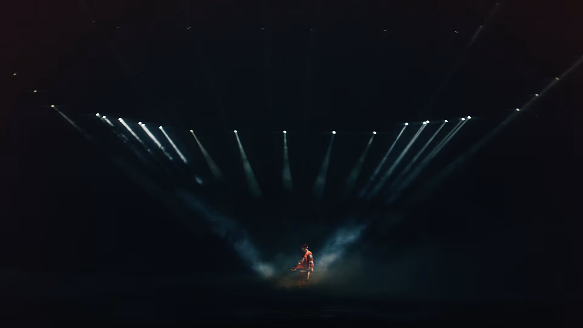 Figure illuminated by multiple spotlights in a dark, smoky environment.