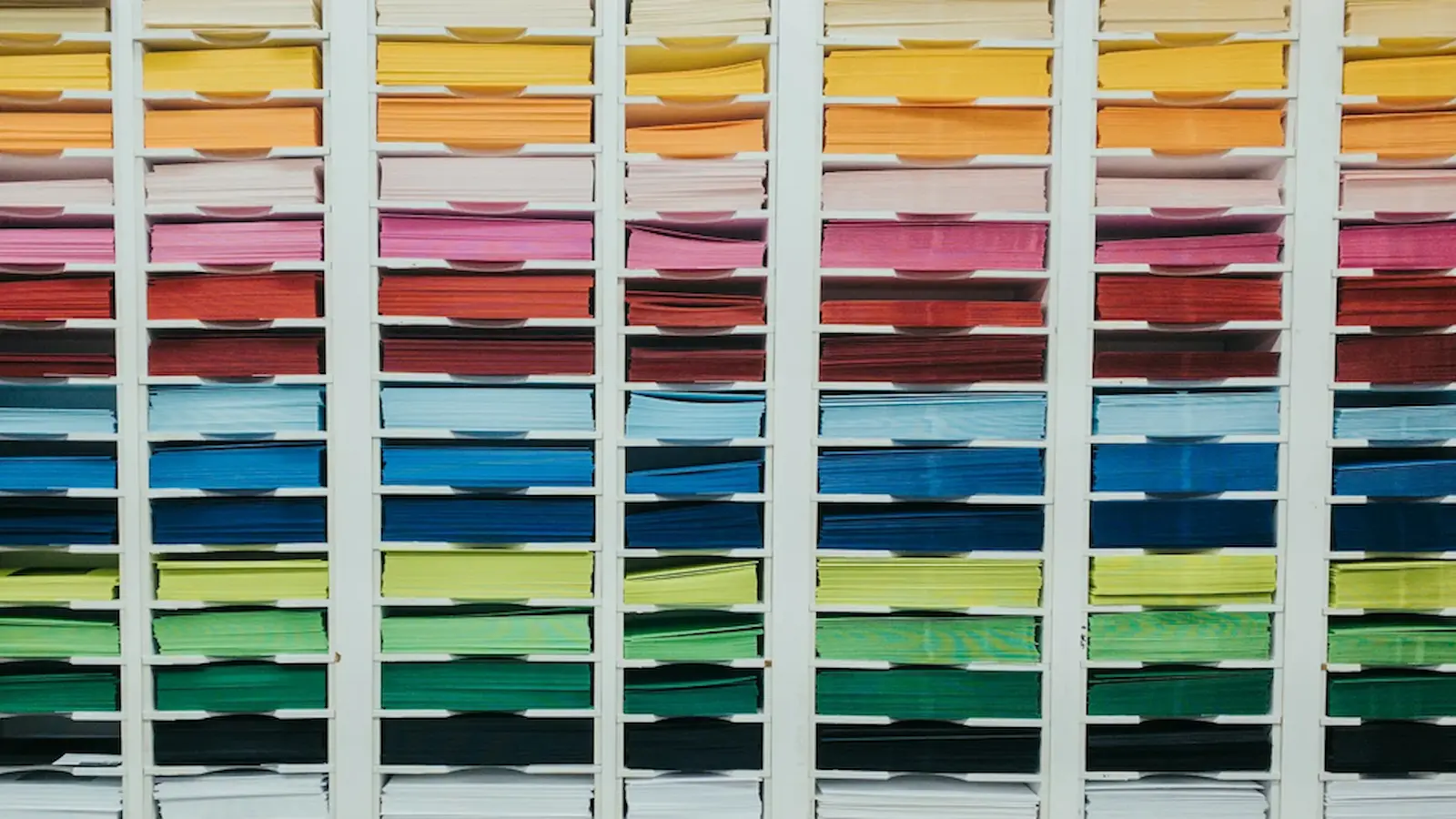 Differently colored and sized stationary organized into various cubbies by color and size.