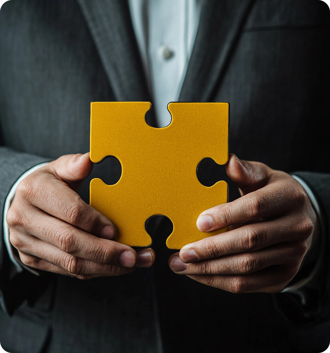 Man in suit holding a large yellow puzzle piece with both hands.