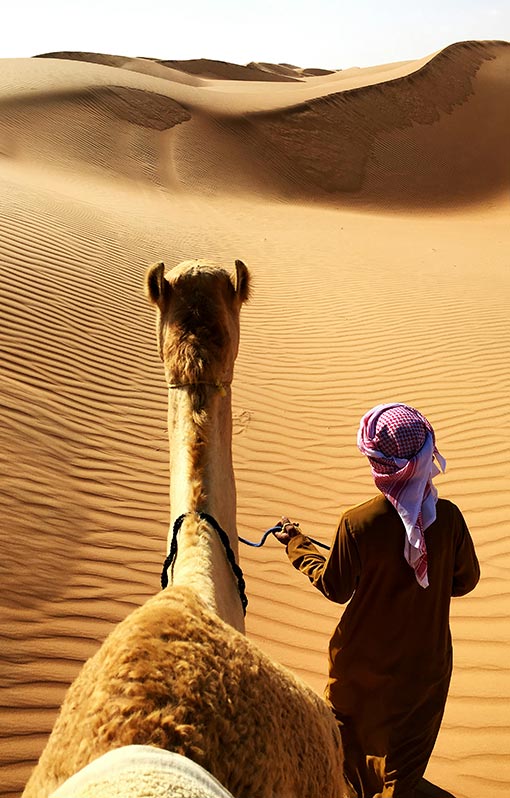 A nomad leading a camel in the desert.