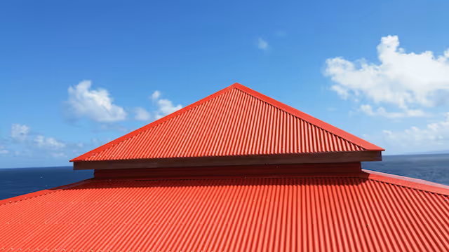 Toit en métal rouge avec ciel bleu et mer en arrière-plan.