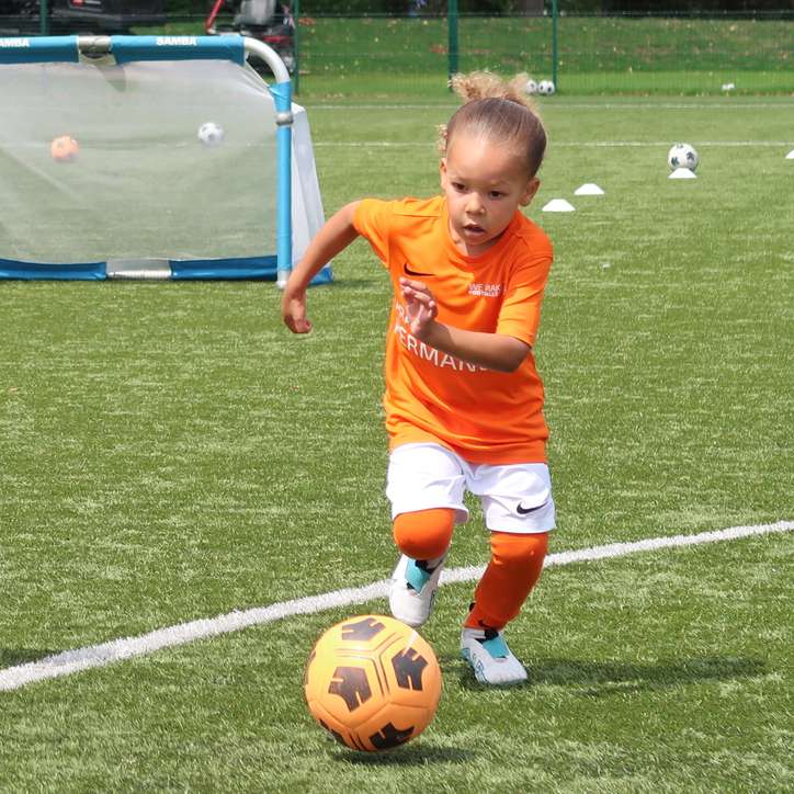girl playing soccer with we make footballers orange jersey