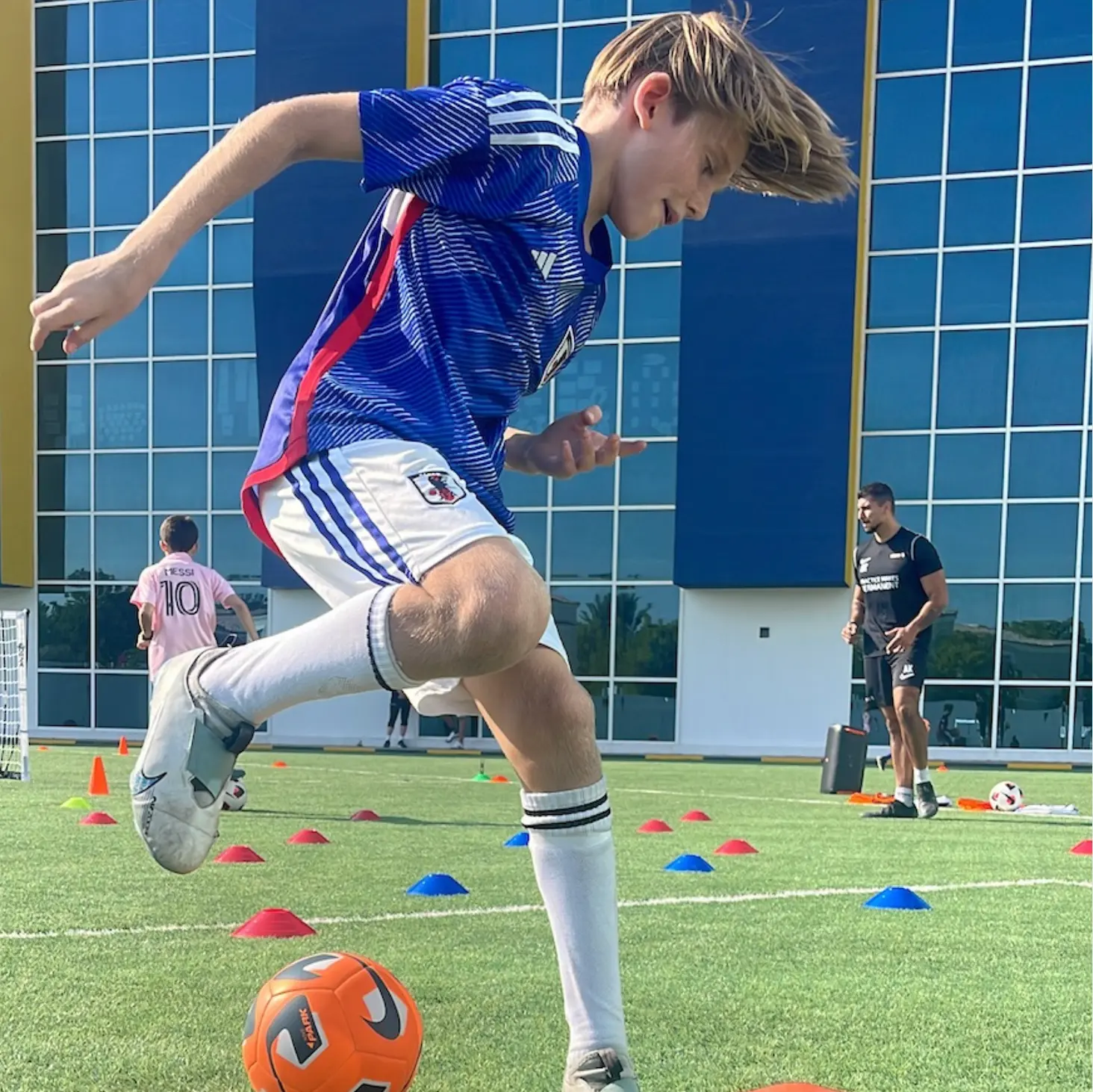 A boy dribbling a football through cones on an outdoor pitch
