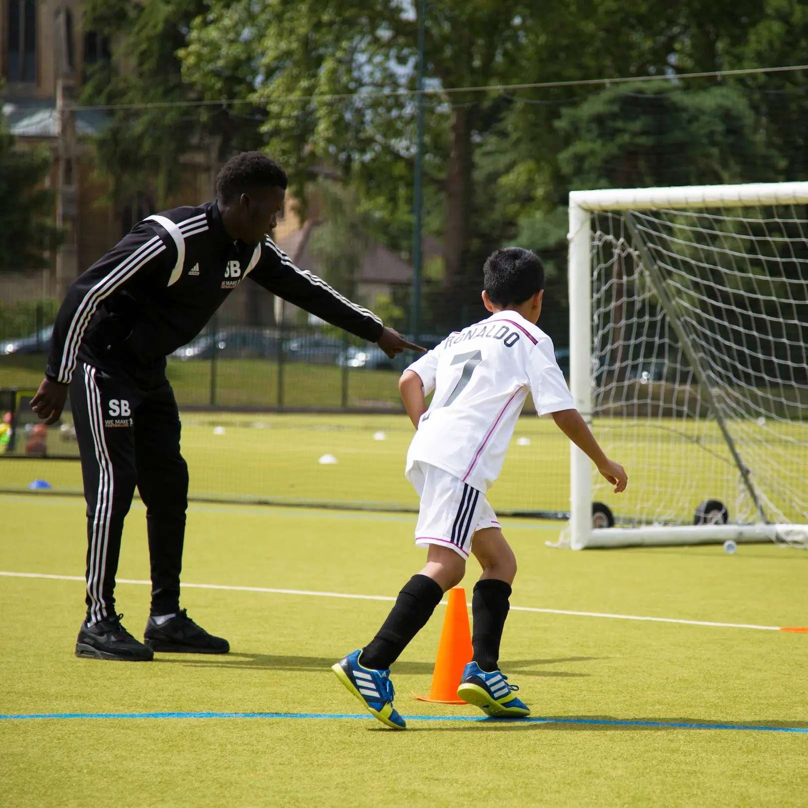 Coach instructing a boy beside a goal on an outdoor football pitch
