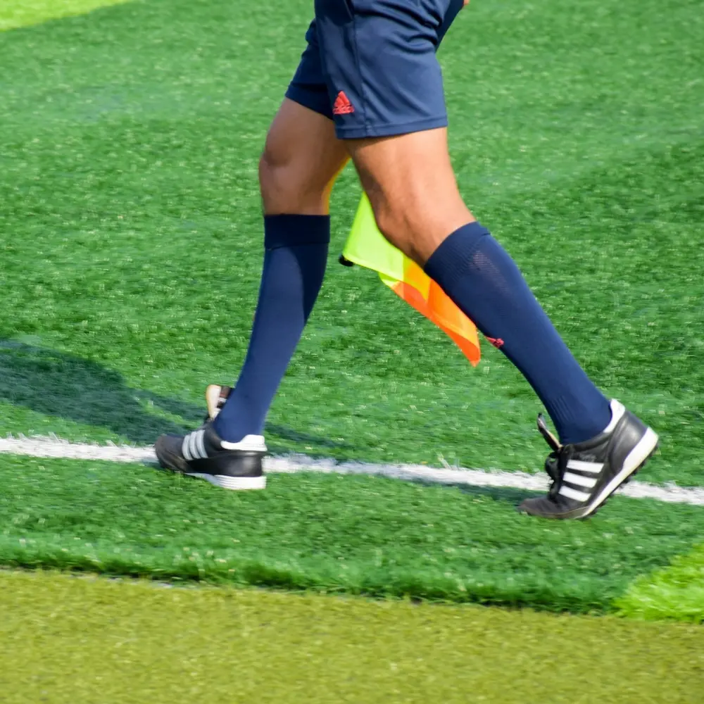 Linesman’s legs and flag running along the touchline on a football pitch

