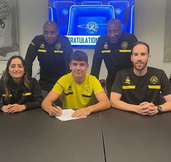 A young player signing a contract, surrounded by coaches and staff in black and yellow sportswear, with a congratulatory screen in the background.