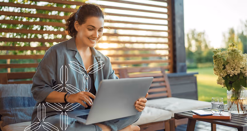 A young woman sits outside on her laptop, smiling.