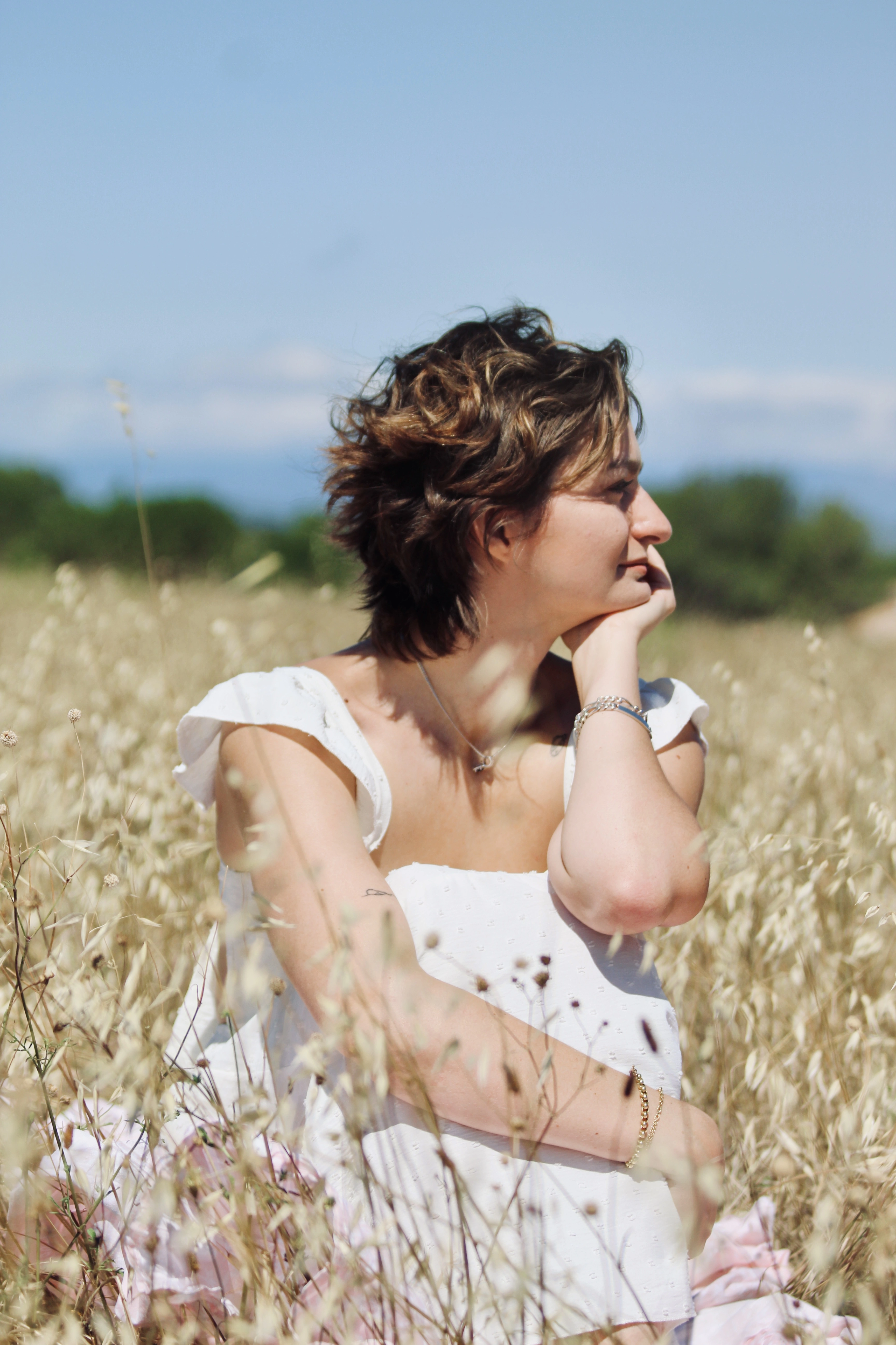 Jeune femme assise dans un champ doré, regardant vers l’horizon, dans une posture calme et introspective.