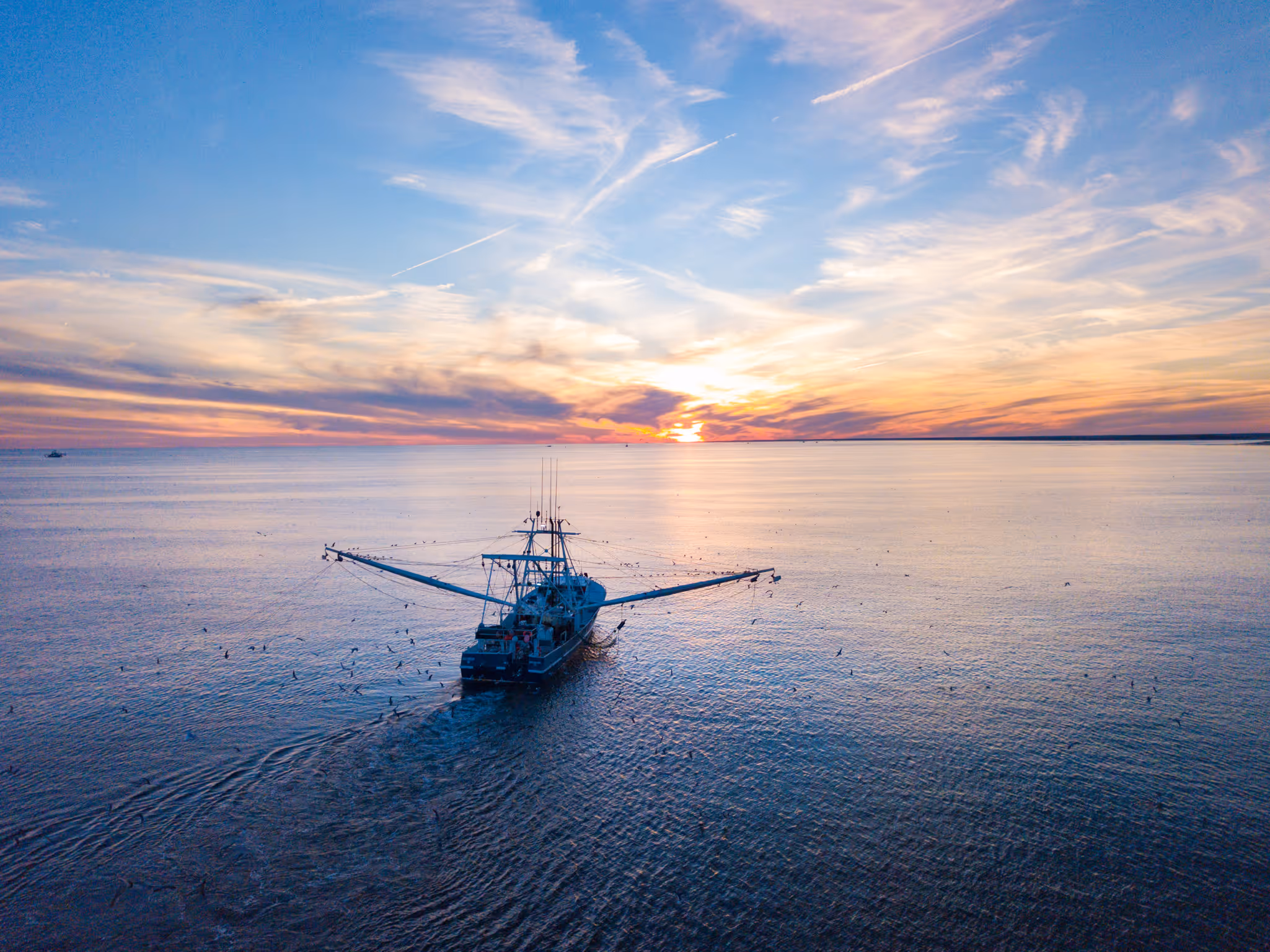 aerial photo of a fishing boat out in the ocean off of north carolinas coast with a sunrise on the horizon