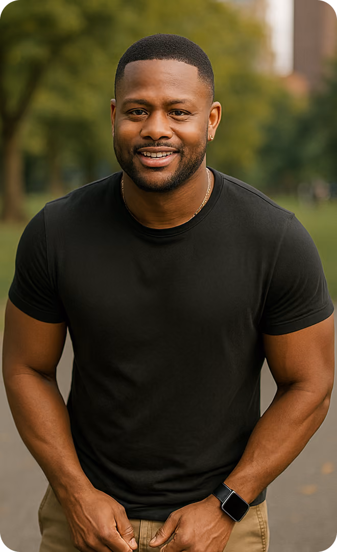 Smiling man with a short haircut and beard wearing a black t-shirt and smartwatch, standing outdoors with blurred trees and buildings in the background.