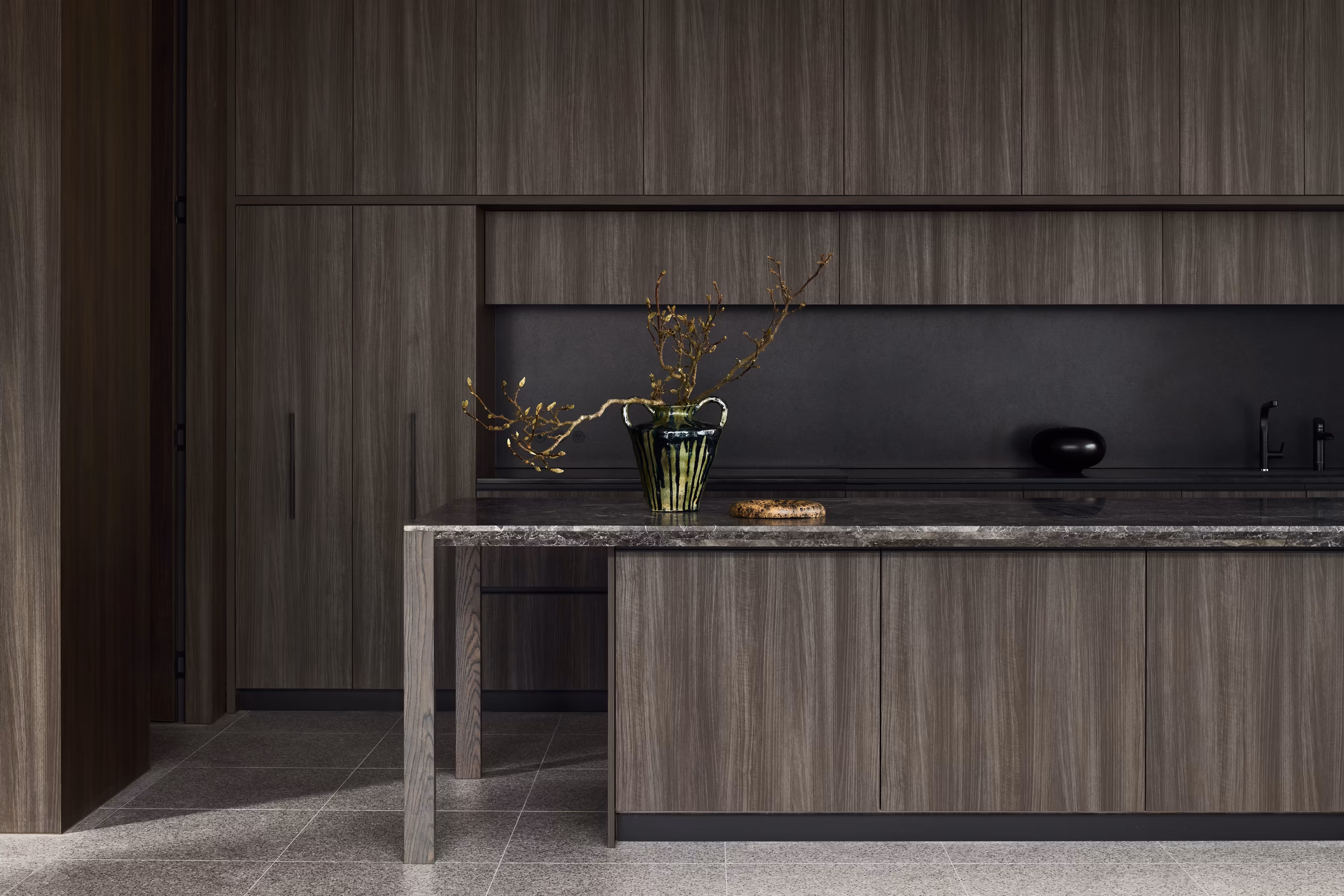 kitchen with dark timber joinery, stone-topped island on timber legs and black splashback
