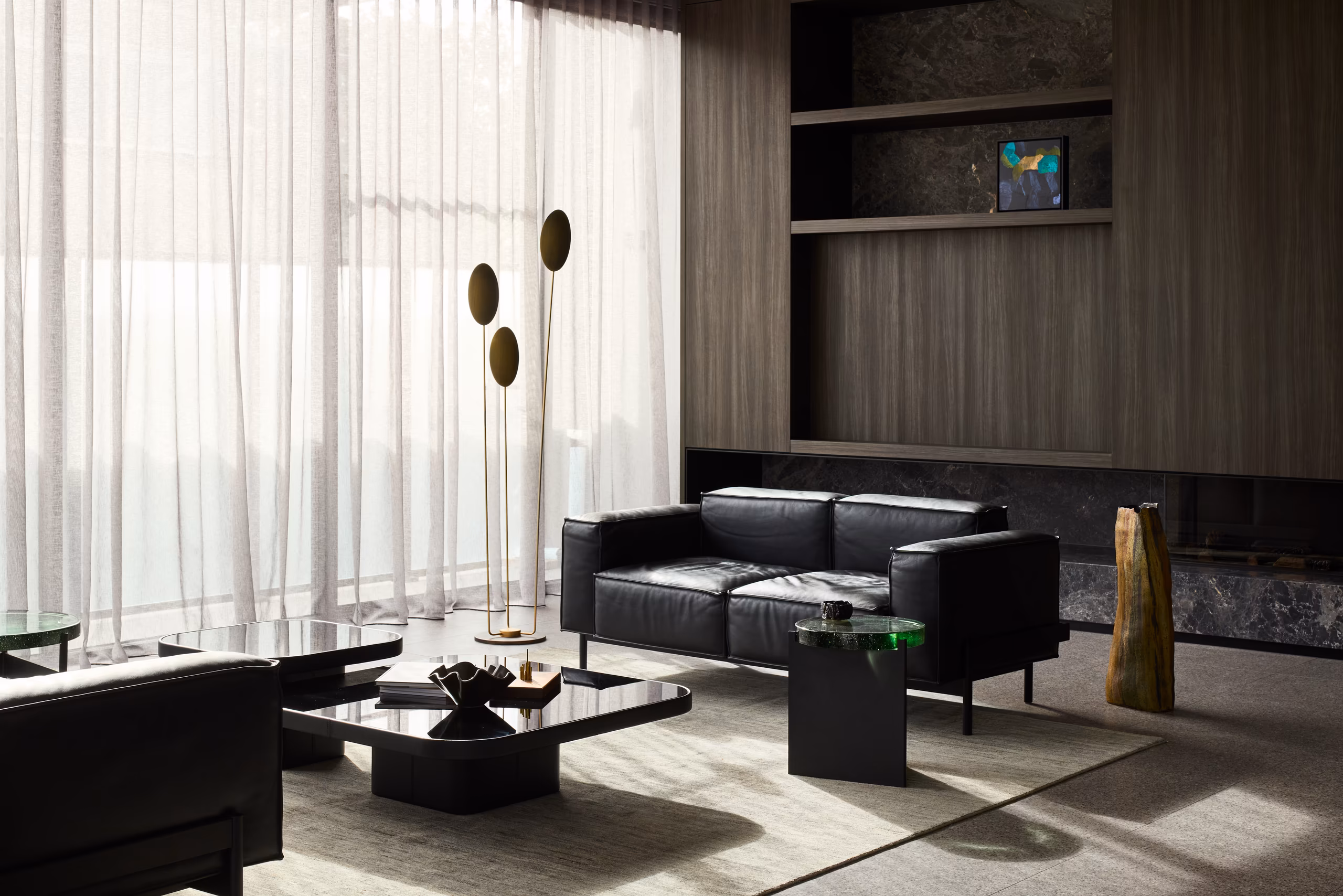living room with black leather sofas, low black coffee tables, brass floor lamp and dark timber joinery