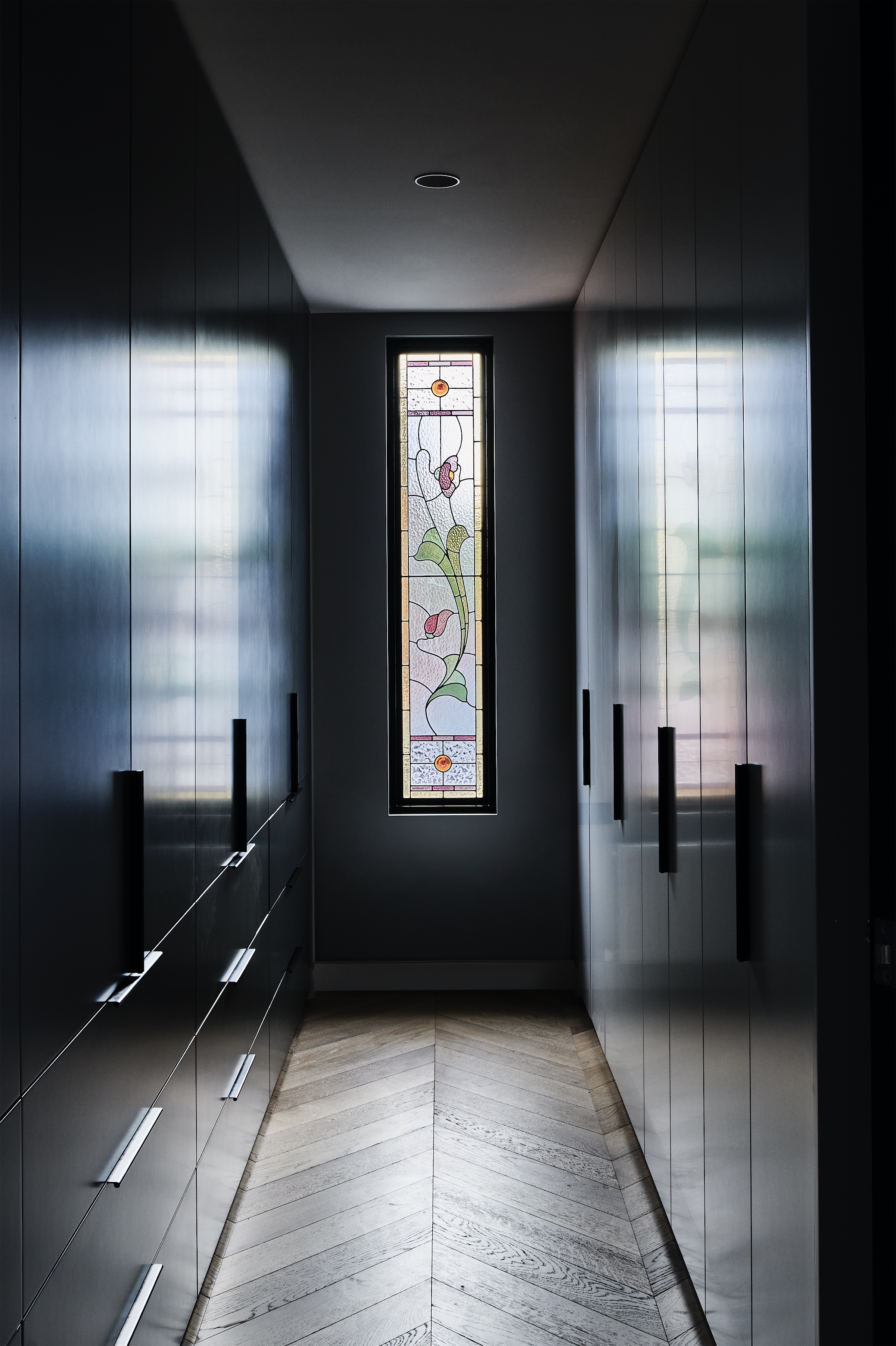 walk-in robe with dark joinery, a leadlight window and chevron timber floor