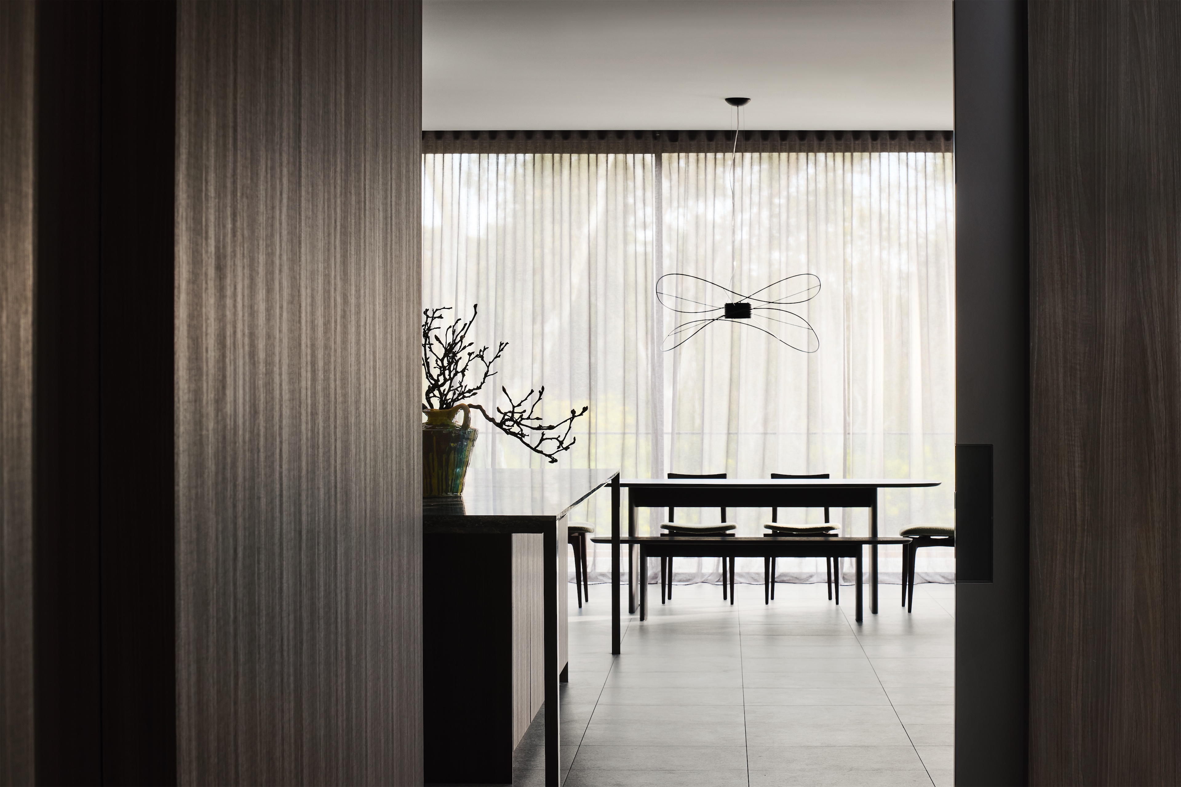 view through a dark timber doorway to the kitchen island and dining table under a wire pendant, opus 24, ashburton