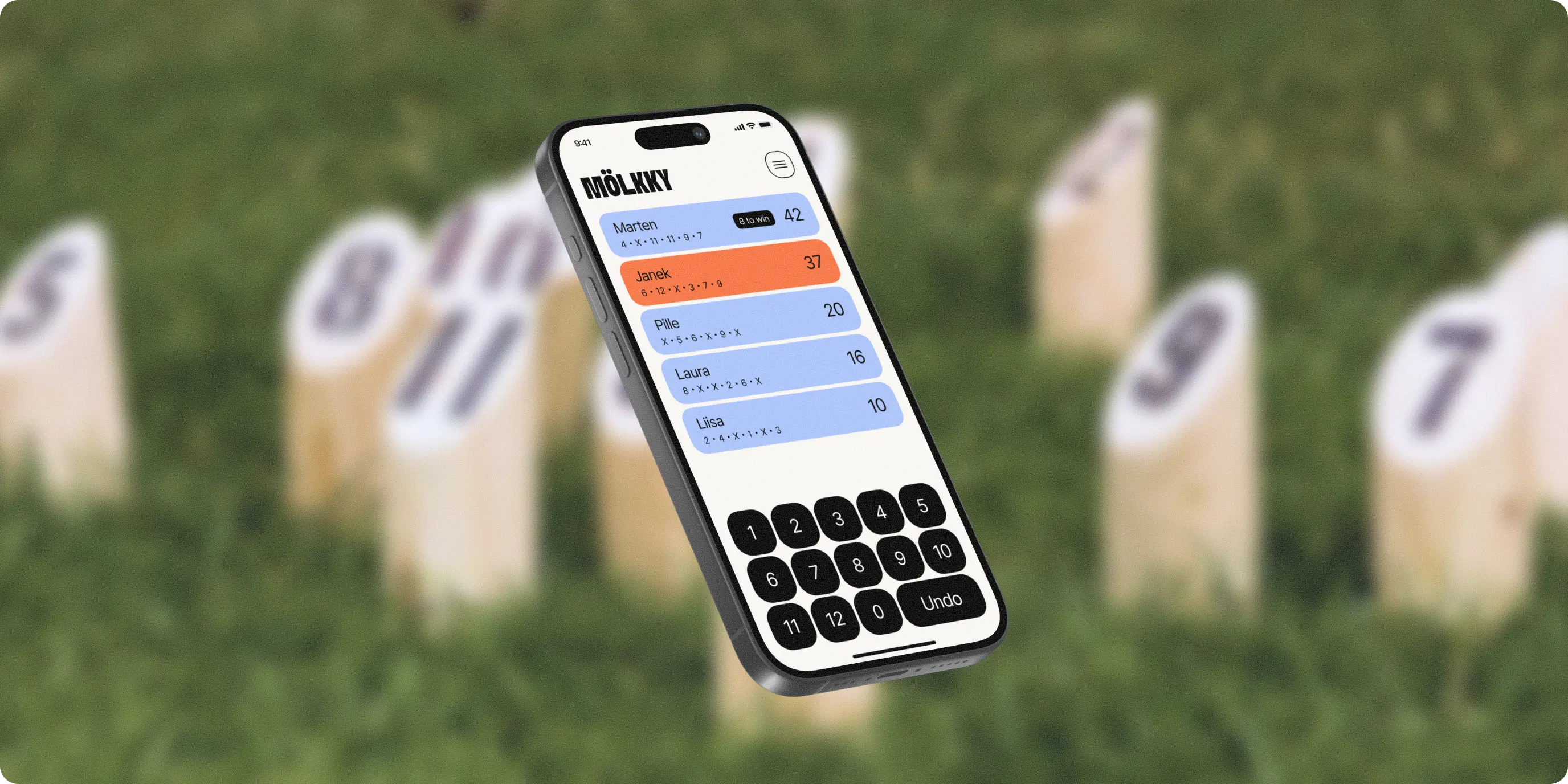Smartphone displaying a Mölkky game scoring app with player scores and a numeric keypad, set against a blurred background of Mölkky wooden pins on grass.