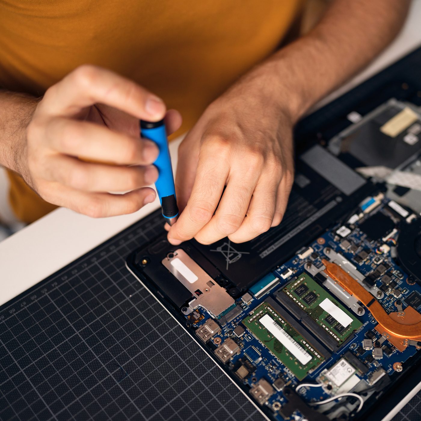 Technicien démontant un ordinateur portable pour réparation, carte mère et mémoire visibles