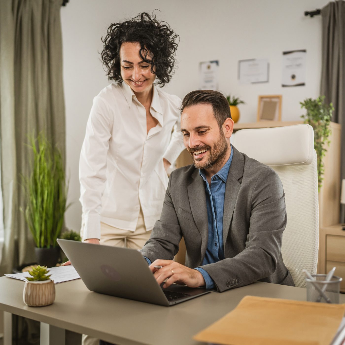 Deux personnes souriantes travaillant ensemble sur un ordinateur portable au bureau