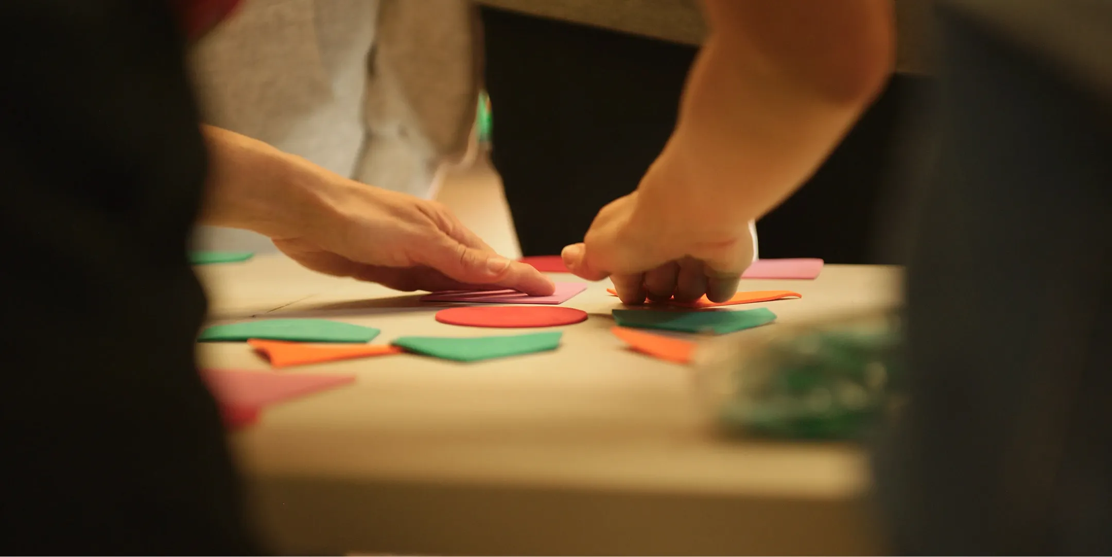 Zwei Hände ordnen bunte Papierformen auf einem Tisch an.