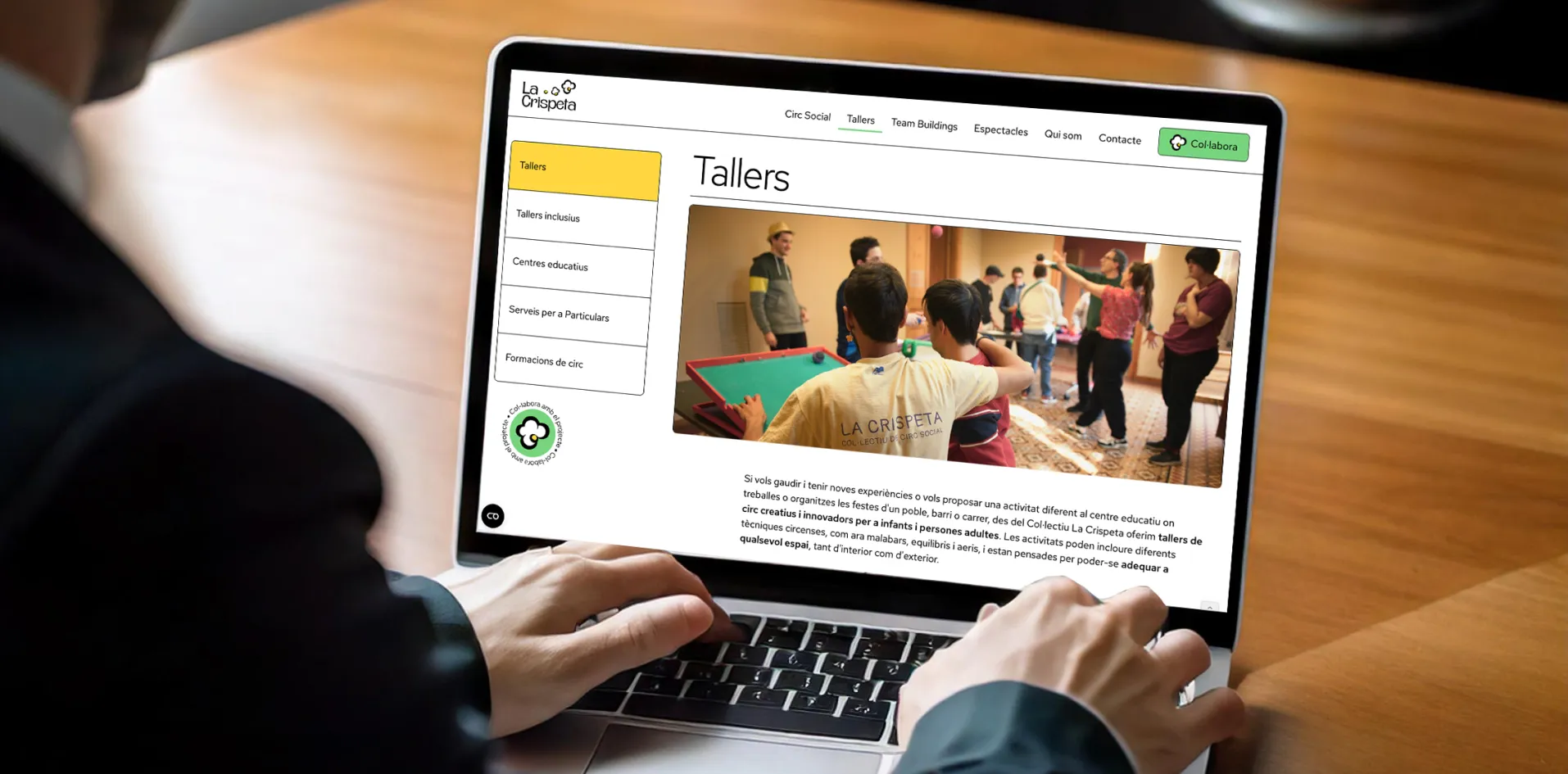 Person sitzt an einem Laptop und sieht eine Webseite mit dem Titel ‚Tallers‘, die eine Gruppe von Menschen zeigt, die an einem Indoor-Workshop mit Zirkustechniken teilnehmen.