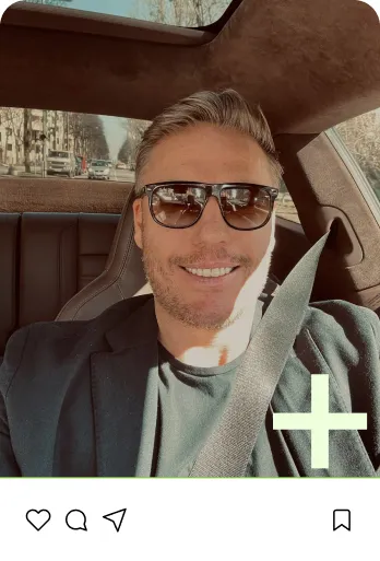 Mann mit Sonnenbrille lächelt im Auto, angeschnallt mit Sicherheitsgurt, Sonnenlicht fällt auf sein Gesicht.