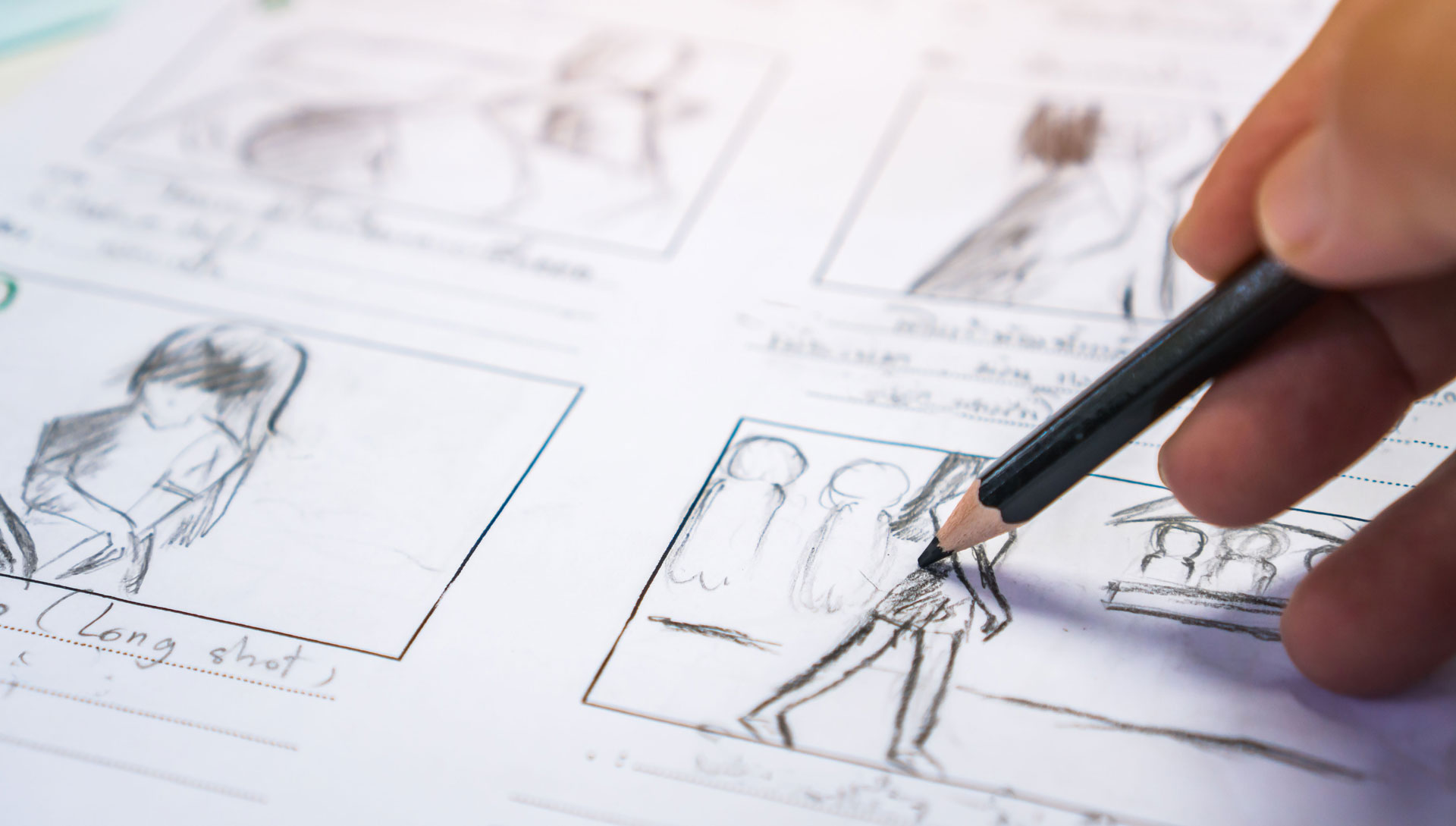 Hand sketching storyboard frames with pencil, illustrating animated characters and scene planning on paper.