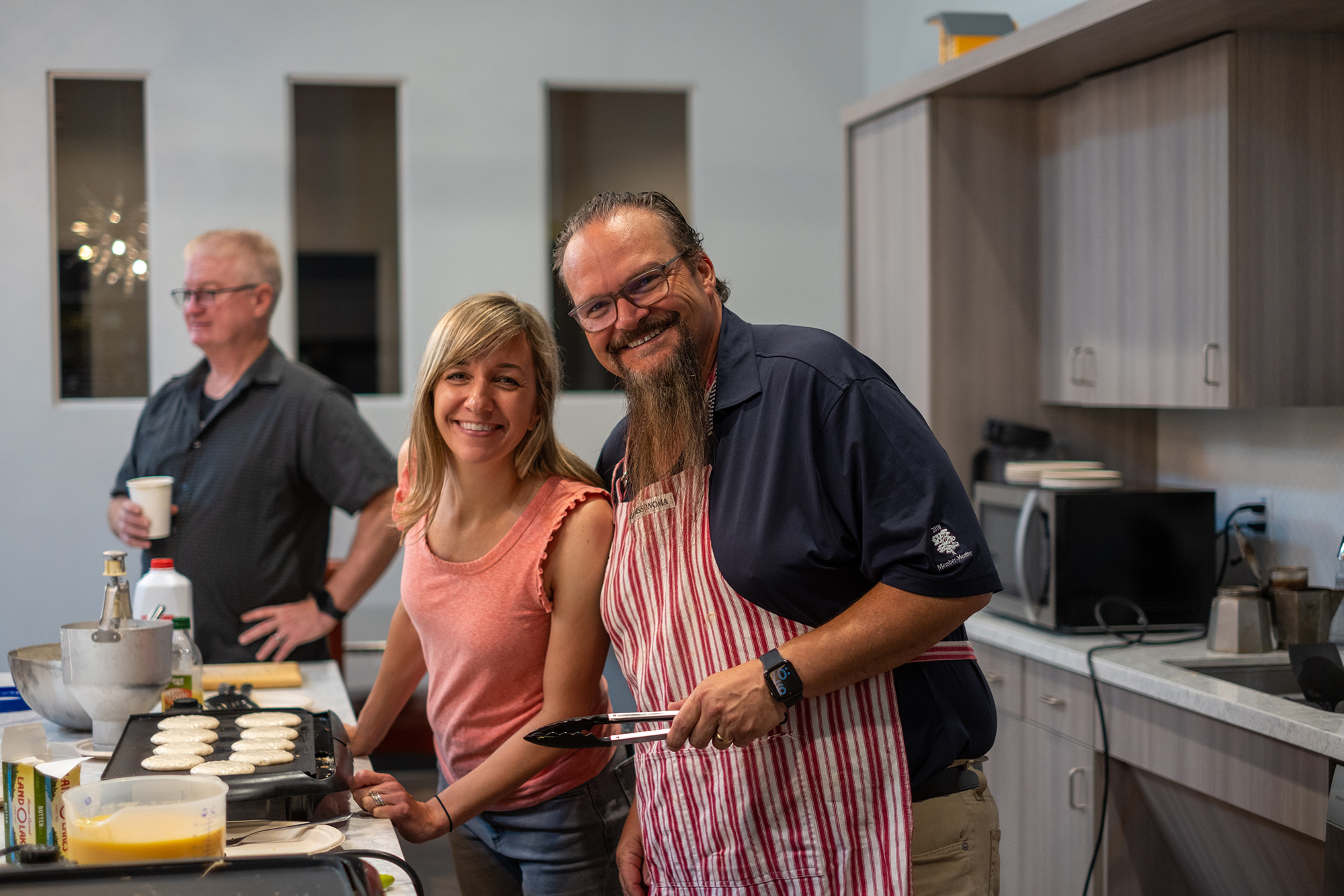 Three people cooking pancakes together in a kitchen.