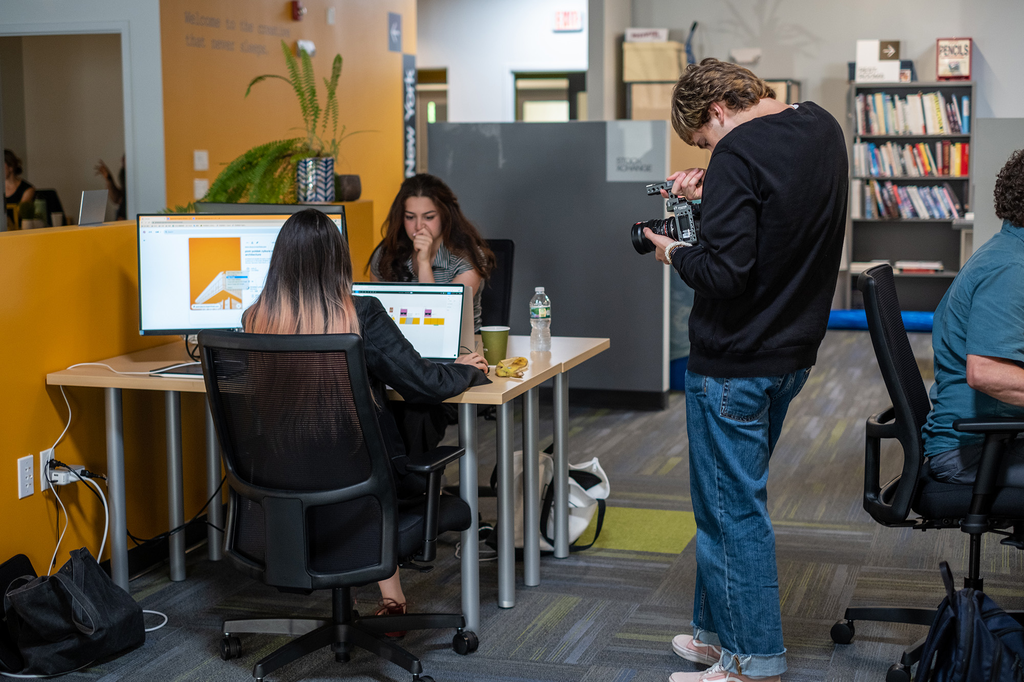 Man photographing two colleagues working at their desks.
