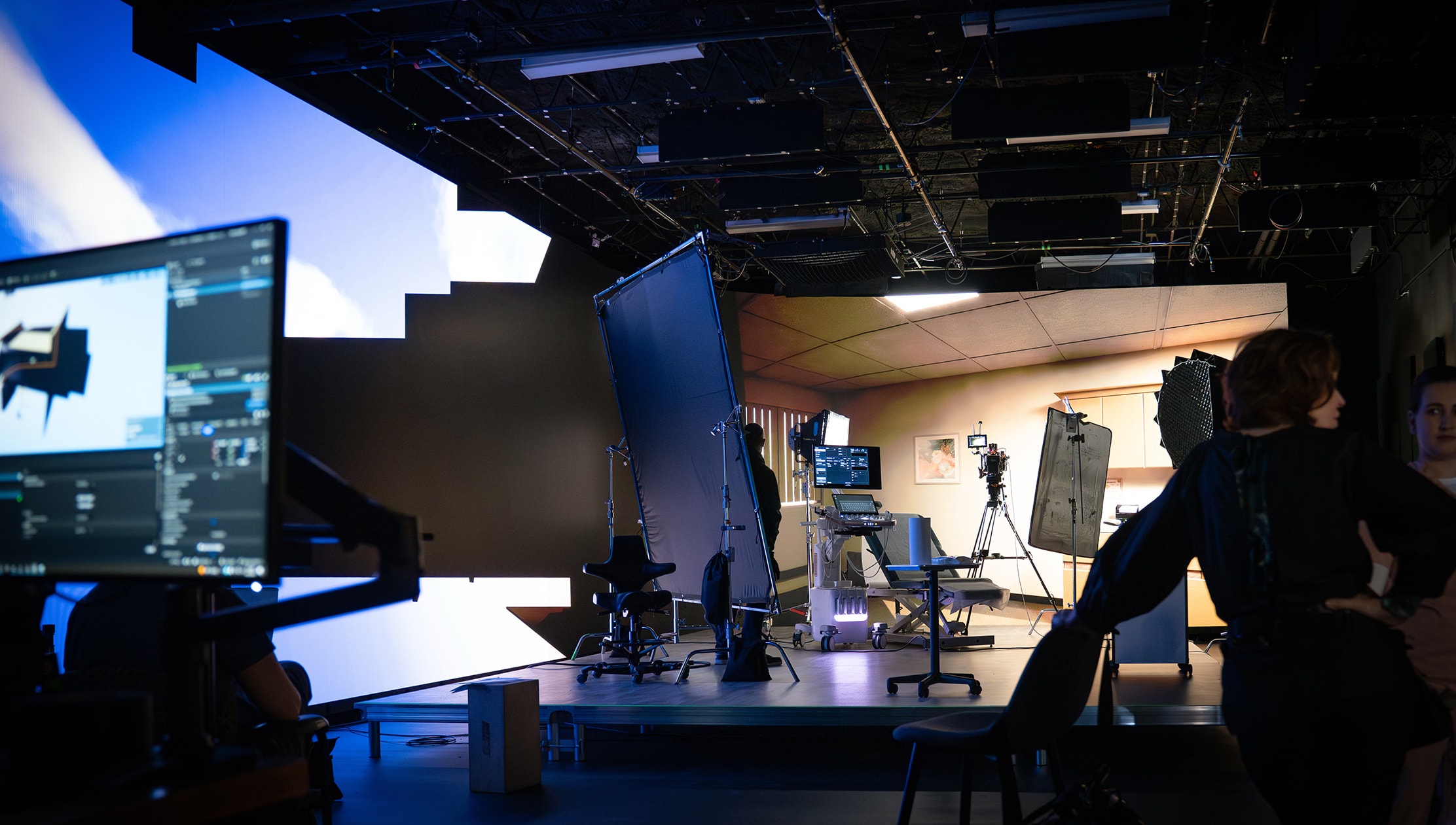 Wide view of a virtual production studio configured as a clinical exam room, with lighting, camera equipment, and LED wall technology visible during a behind-the-scenes video shoot.