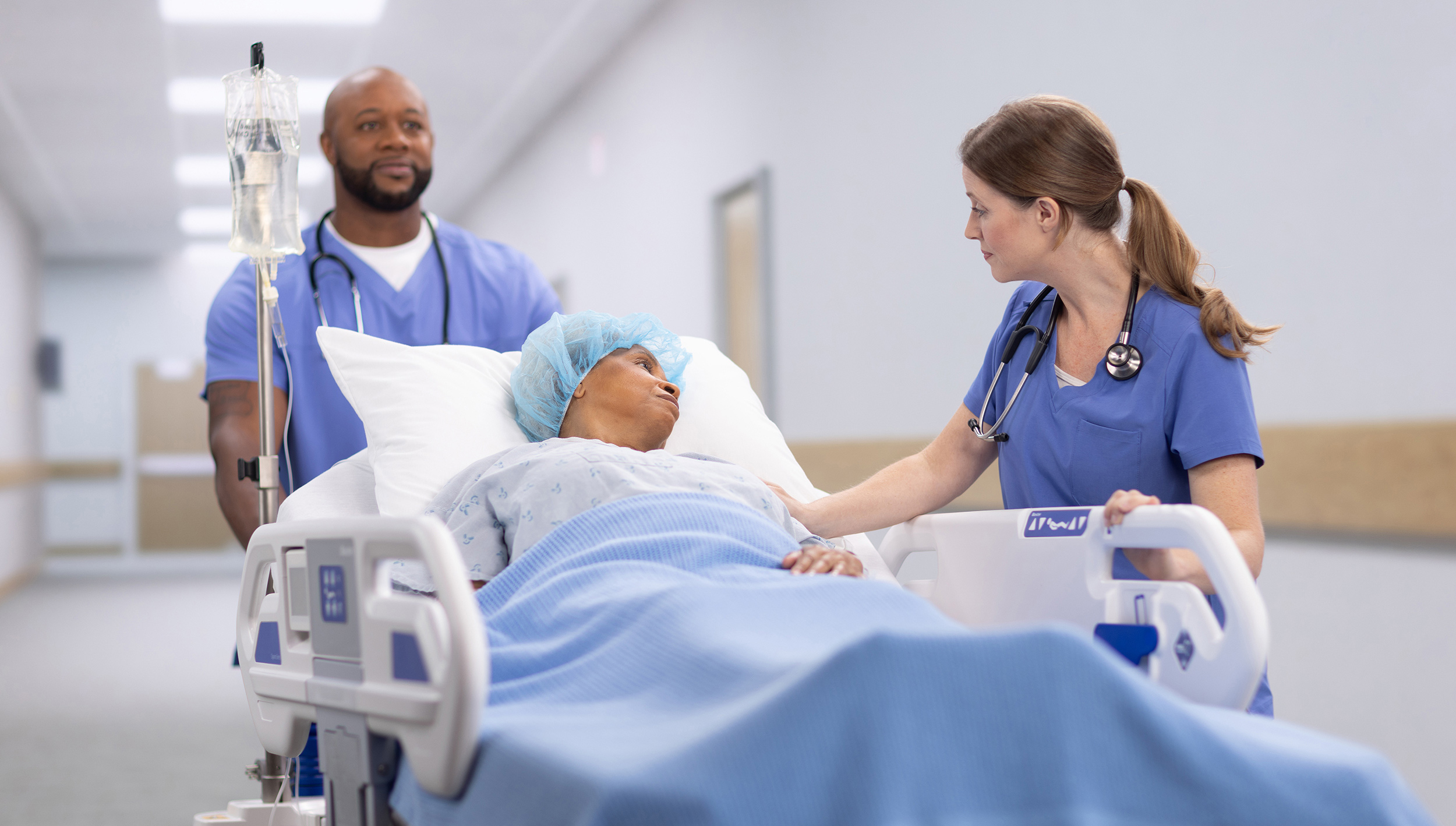 Behind-the-scenes hospital set with lighting equipment, crew, and a patient bed staged in a clinical hallway.