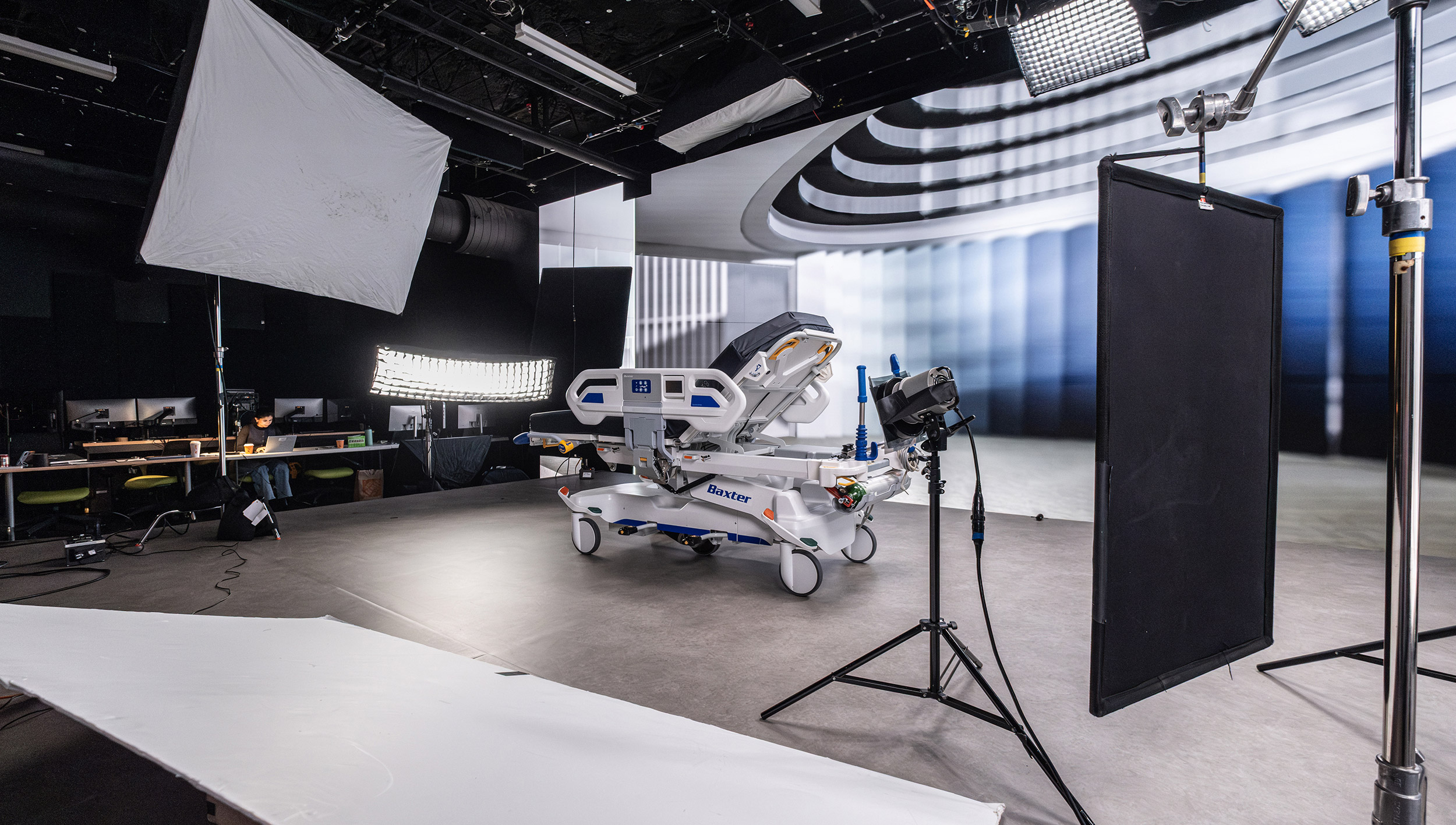     Behind-the-scenes studio setup featuring a hospital bed, large lighting rigs, screens, and production equipment.