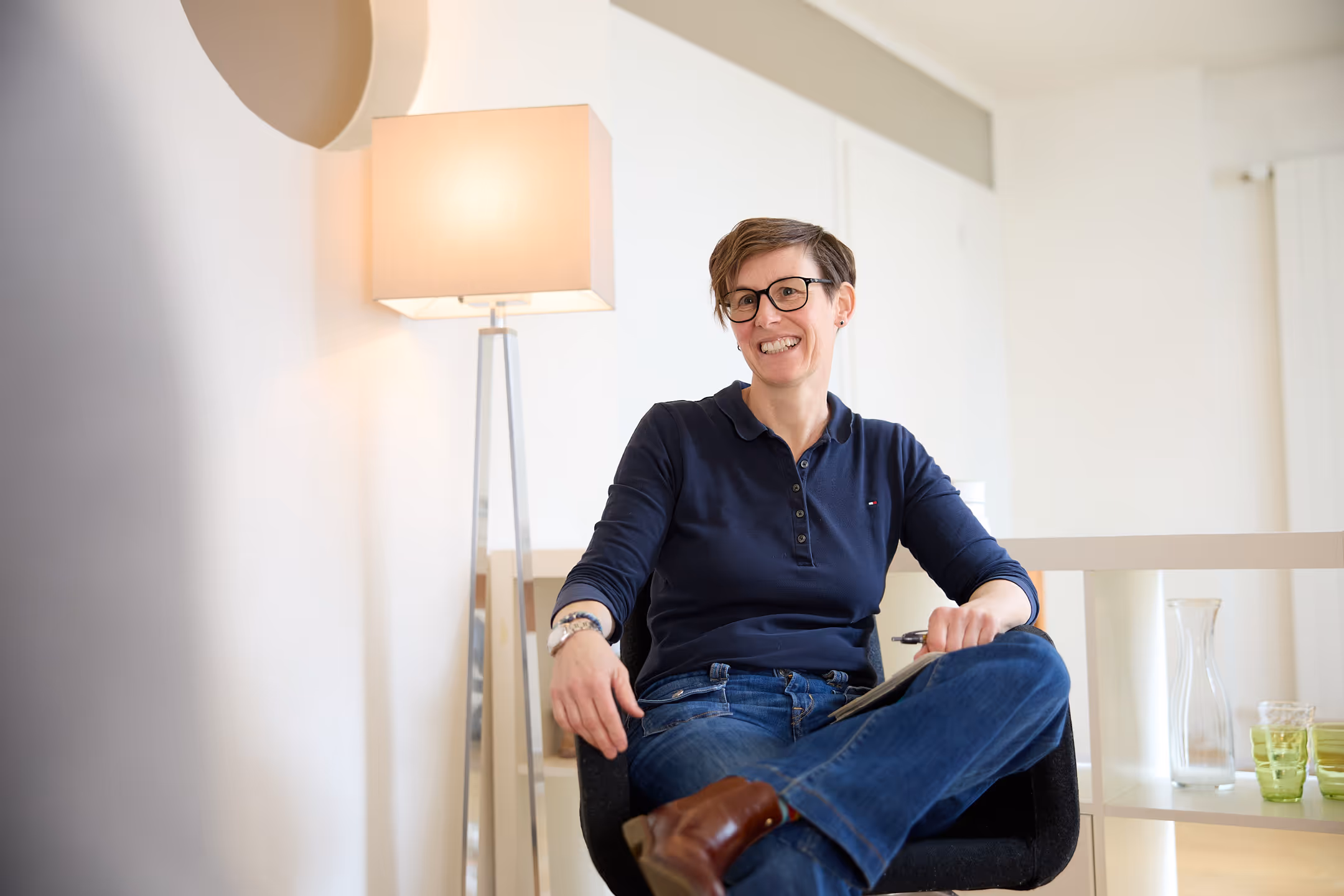 Nadia Lehnhard sitzt auf einem Stuhl neben einer Stehlampe und hört aufmerksam zu