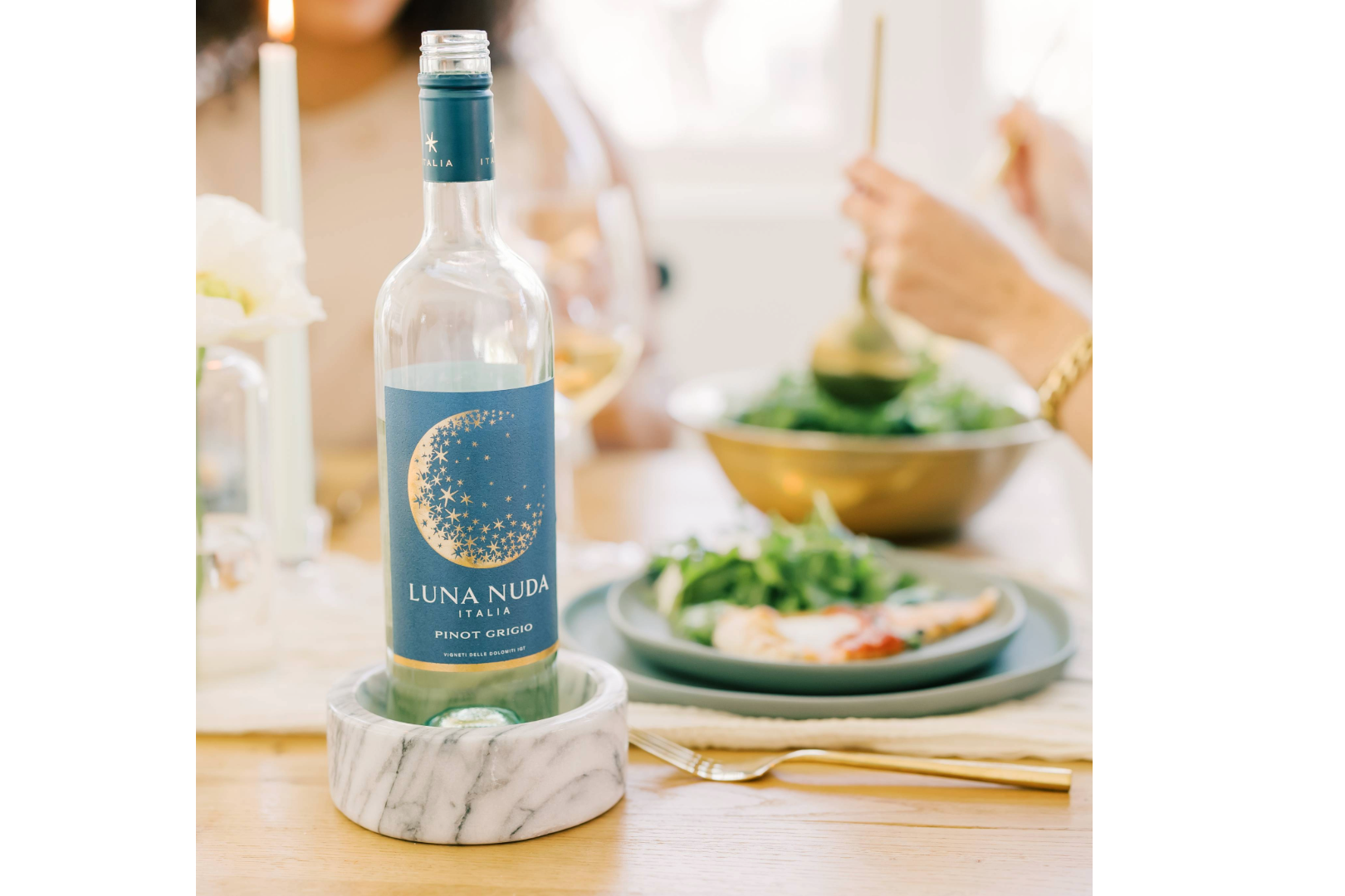 Bottle of Luna Nuda Pinot Grigio on a marble coaster at a dinner table with a green salad