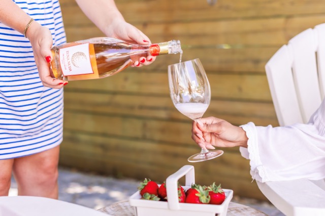 Pouring a glass of Luna Nuda Rosé on a patio table with a basket of fresh strawberries