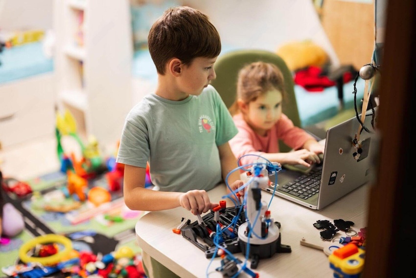 Bay Area students collaborating on a competitive youth robotics build, utilizing a coding laptop and mechanical components at a work table