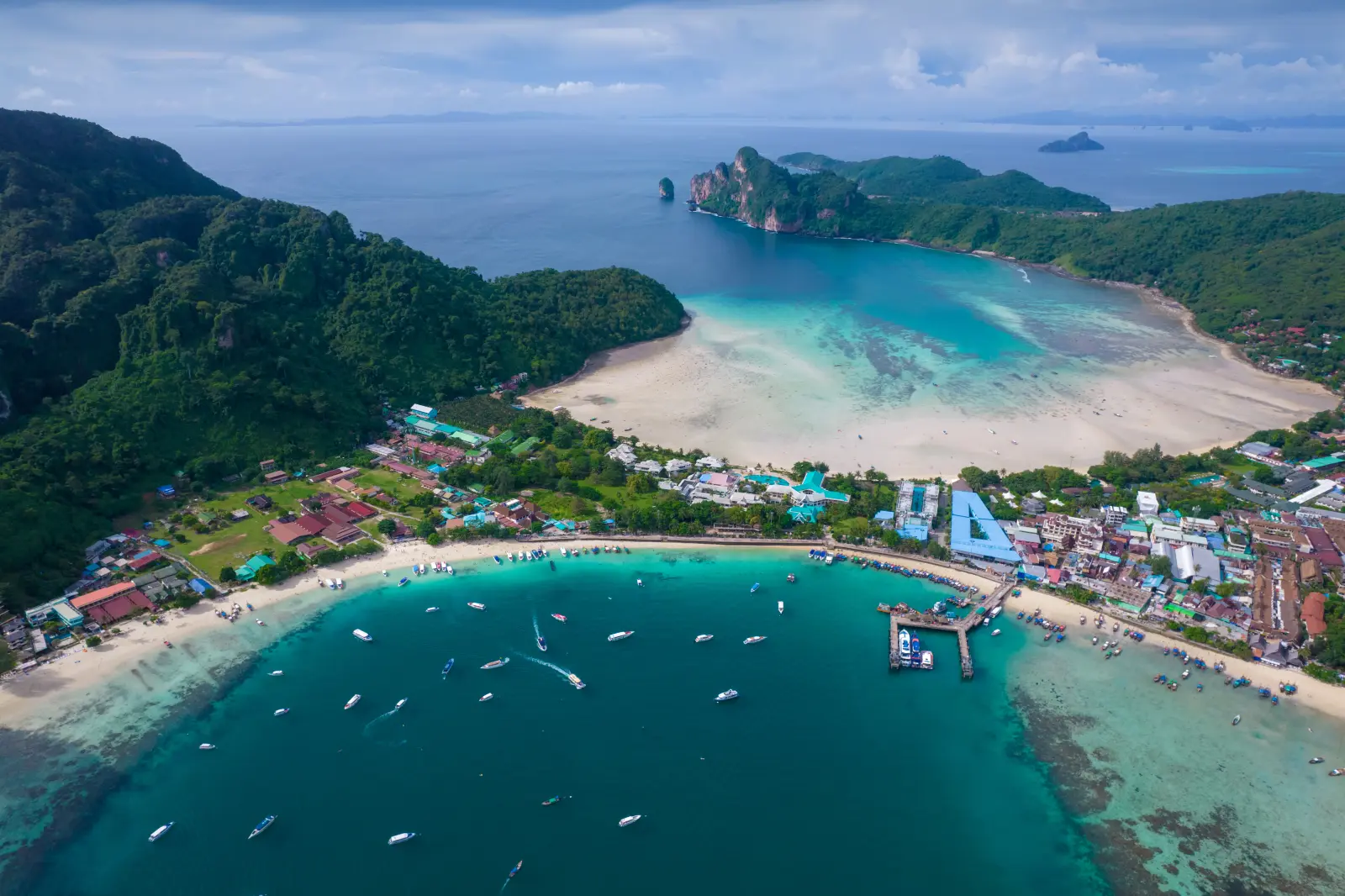 Aerial view of Phi Phi Don Island in Thailand with turquoise bays, white-sand beaches, boats, and lush green limestone hills.