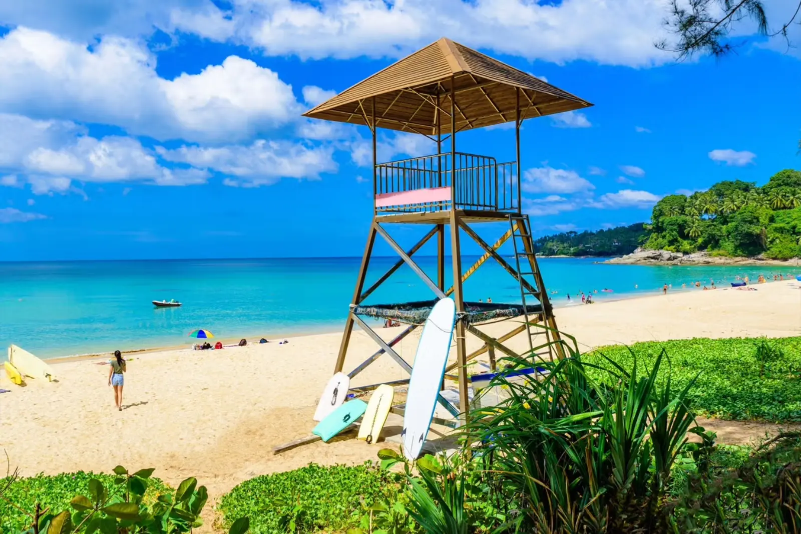 Surin Beach in Phuket, Thailand, with turquoise water, golden sand, a lifeguard tower, surfboards, and tropical greenery.