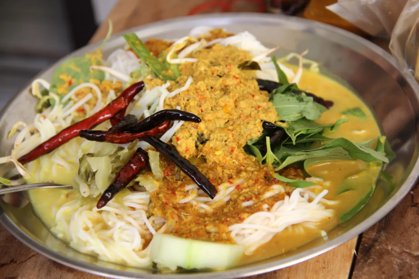 Khanom jeen Thai rice noodles served with rich curry sauce, fresh vegetables, herbs, bean sprouts, and dried chilies.
