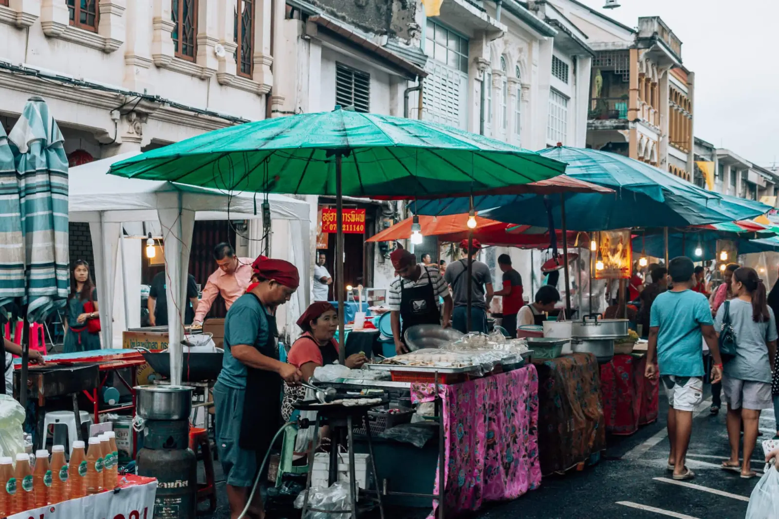 Street food market in Phuket Old Town with local vendors, colorful umbrellas, and visitors along a historic Sino-Portuguese street.