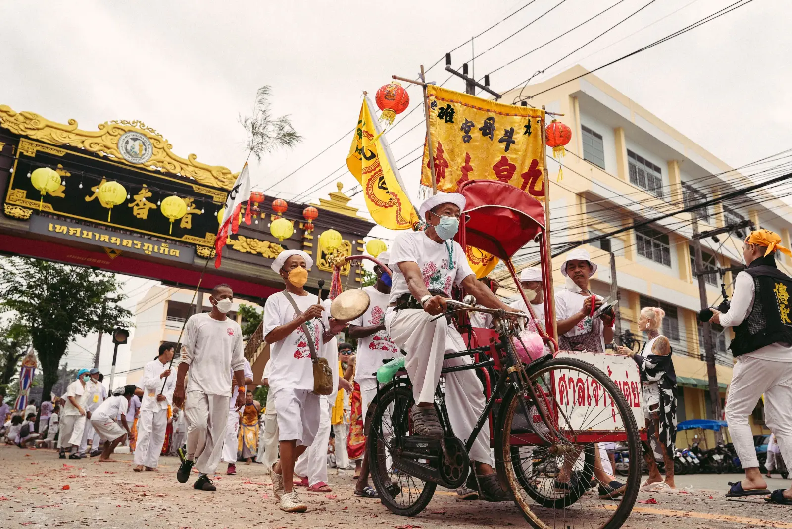 Participants in the Phuket Vegetarian Festival procession wearing white clothing and carrying ceremonial banners near a Chinese shrine in Phuket, Thailand.
